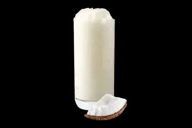 A glass of Coconut Dream Freeze drink with a slice of coconut in front on a transparent background.