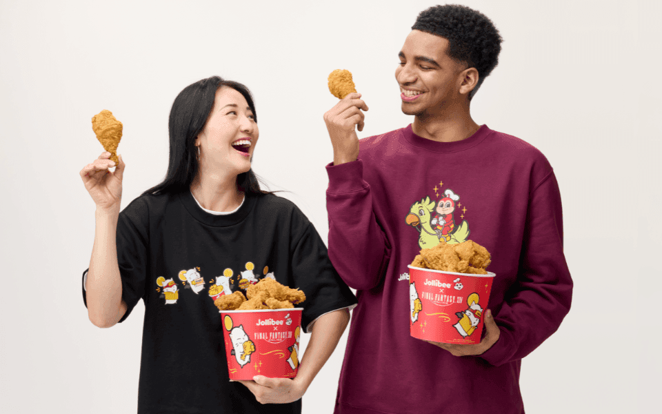 Two people smiling wearing Jollibee merch and holding a bucket of fried chicken.