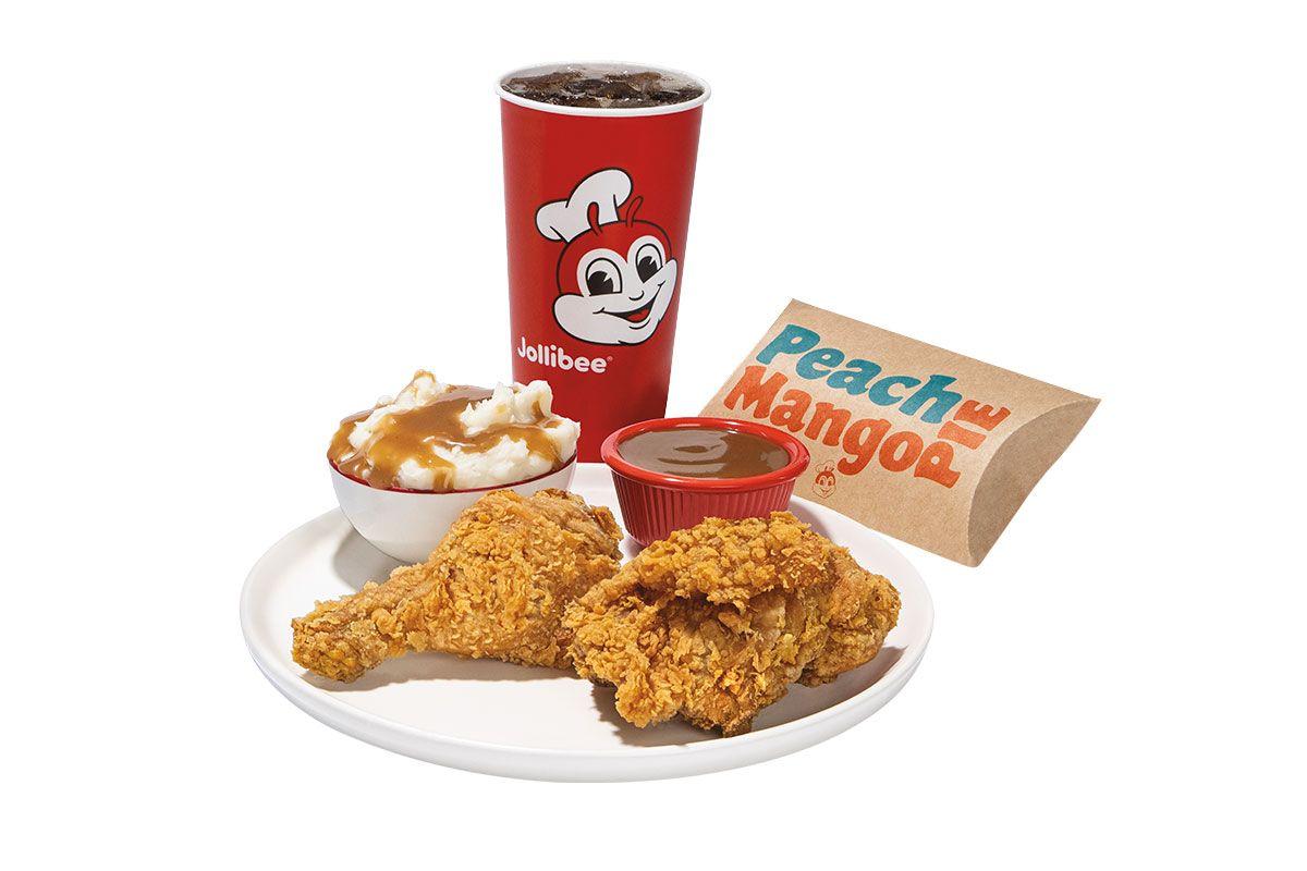 Two pieces of fried chicken with mashed potatoes and gravy on a plate with a drink and pie on a white background