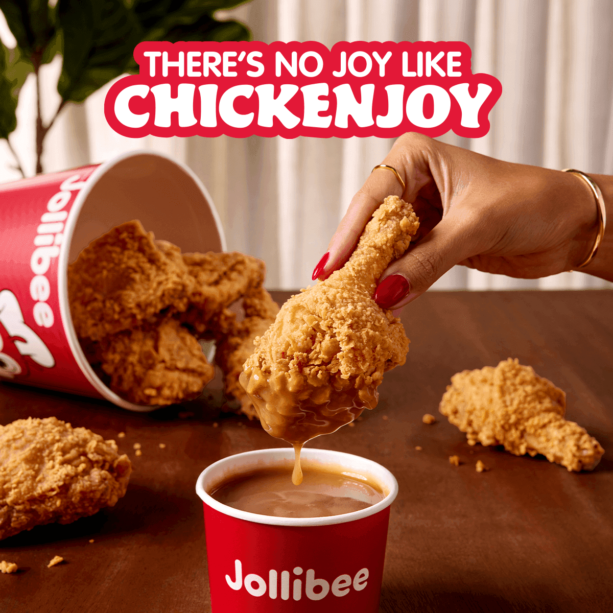 A bucket of fried chicken tipped over and a hand holding a drumstick dipped in gravy with 'There's no joy like Chickenjoy' text.